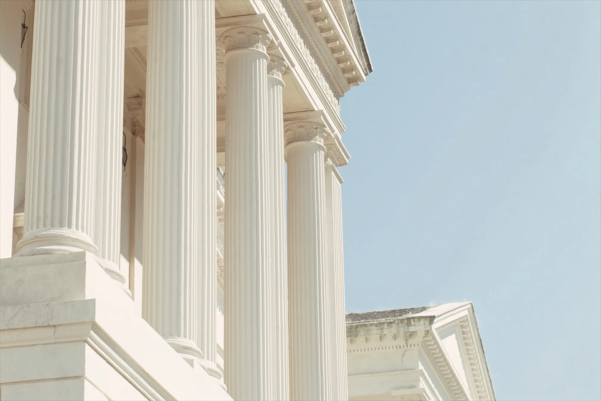 Tall classical limestone columns of a civic building against a clear blue sky in bright sunlight