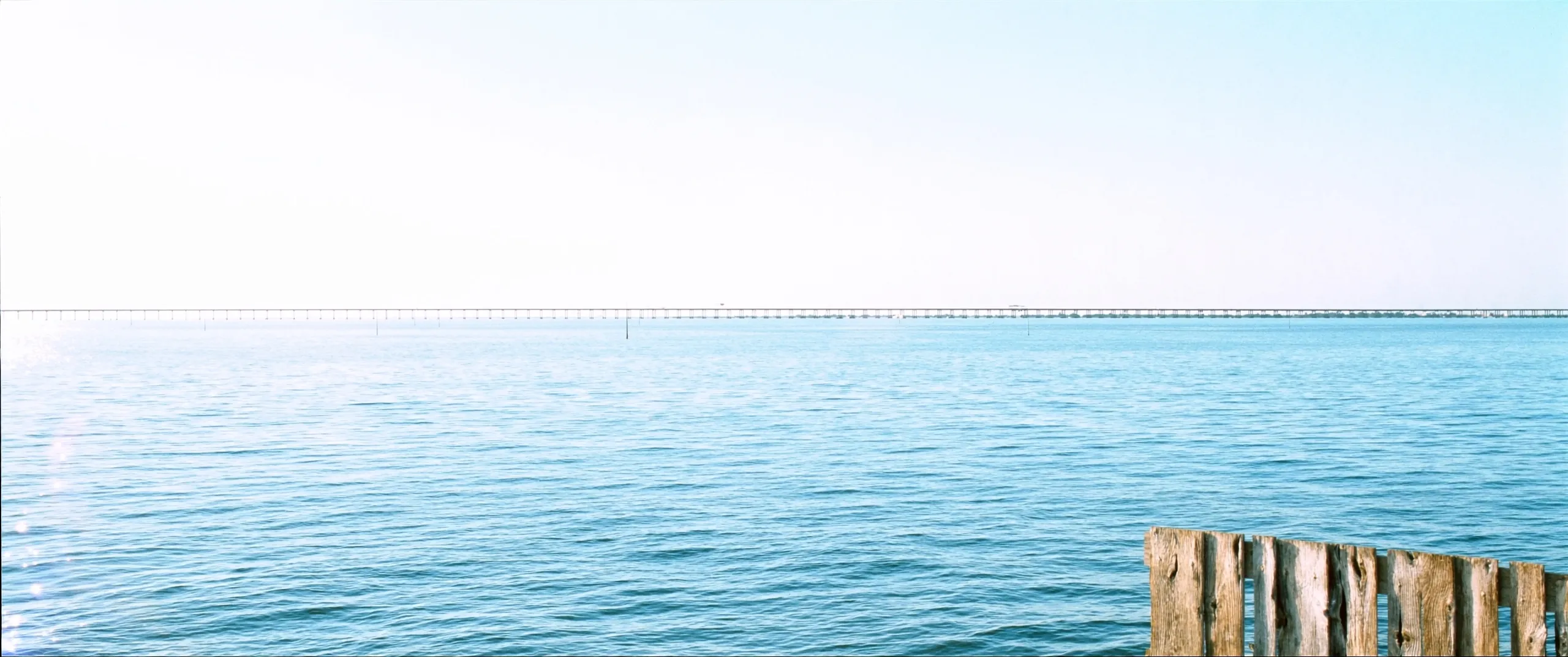 Lake Pontchartrain in bright morning light, the causeway faint on the horizon beyond calm blue water